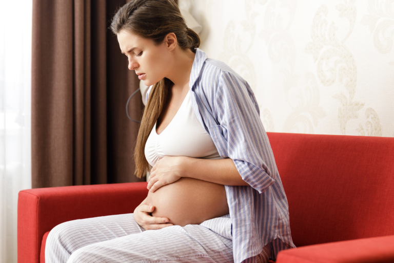 Pregnant mum sitting on red sofa holding her tummy