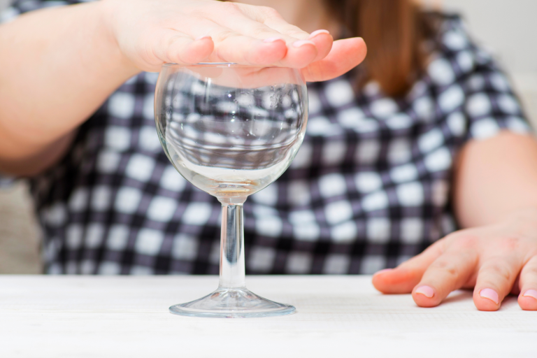 Pregnant lady covering he top of a wine glass with her hand