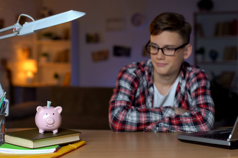 Teenage boy at desk looking at piggy bank