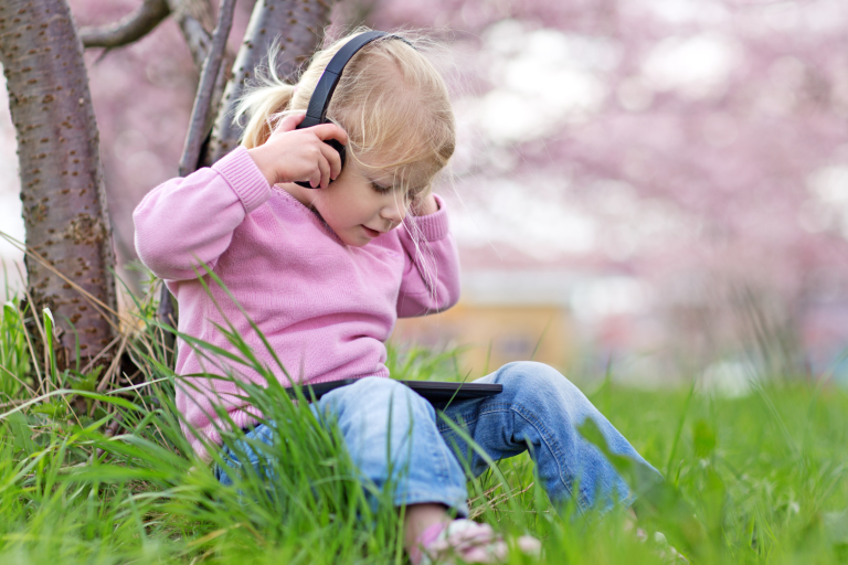 Toddler with ear phones on sitting on lawn watching device