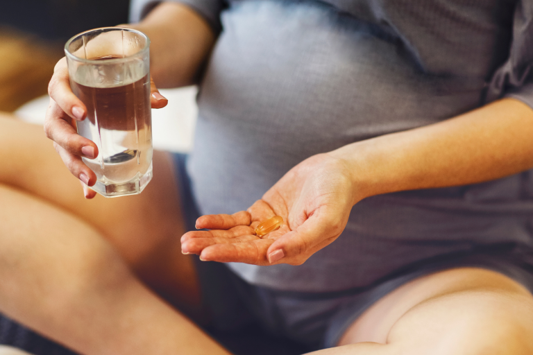 Pregnant mum holding a vitamin in one hand and glass of water 