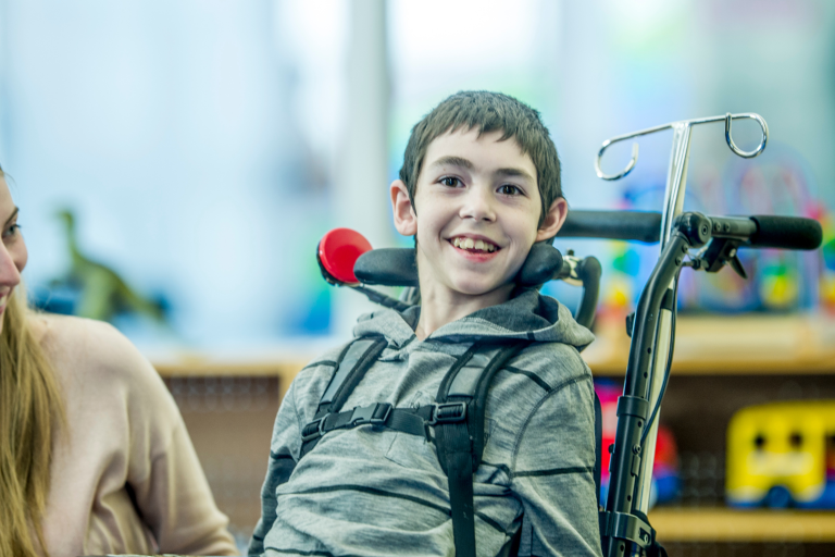 A woman and a boy in a wheelchair smiling, in an educational setting.
