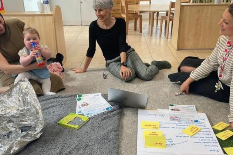 Three adults talking and watching a child play