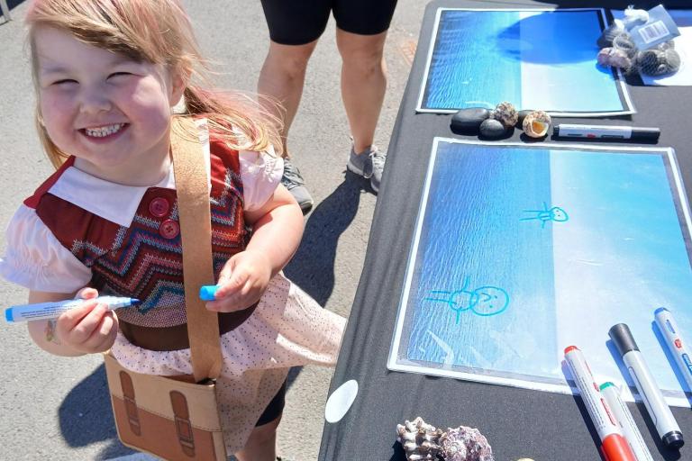 Child smiling at the camera whilst drawing a picture