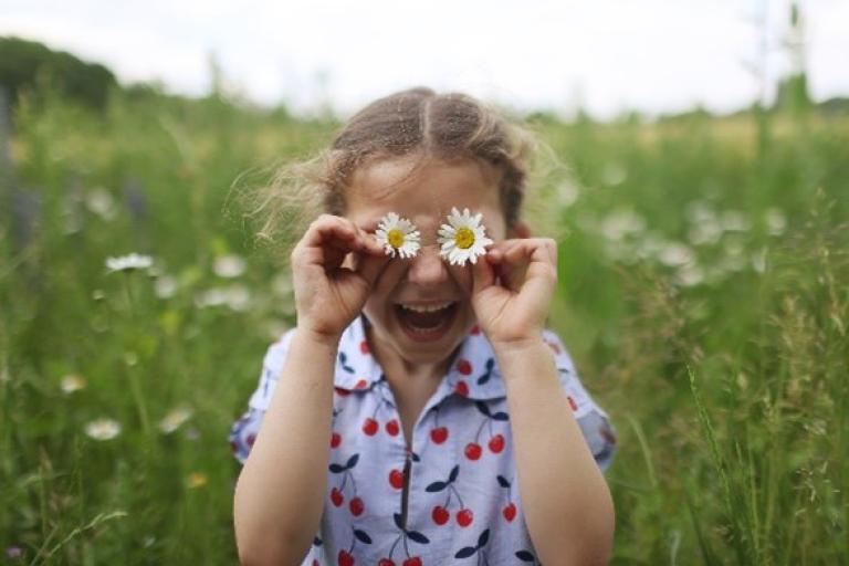 Child using daisies as eyes, playing in a field