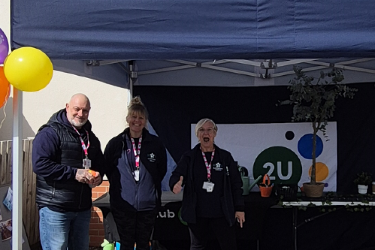 Three adults from the Hub2U team, stood in front of a stand outside
