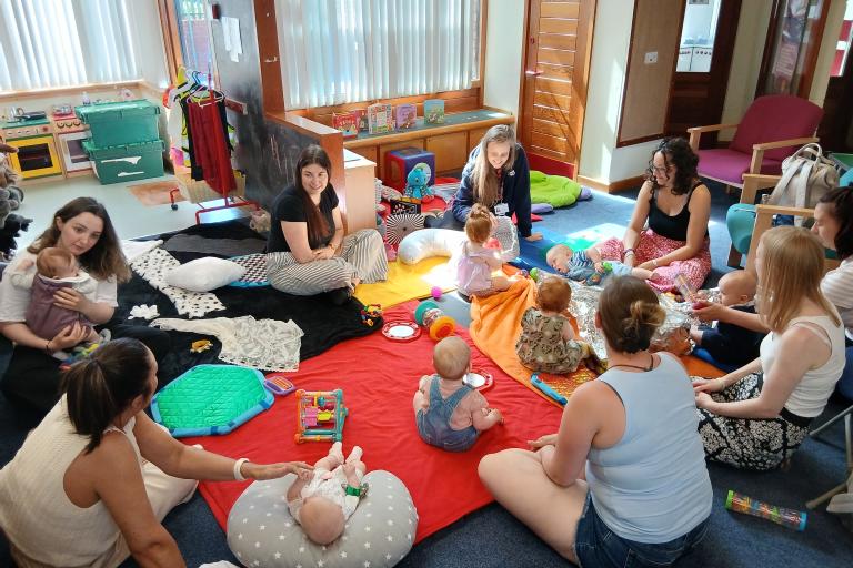 Group of women sat on the floor with babies playing