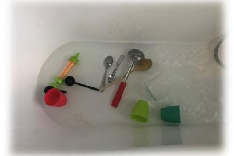 Different sized spoons and cups in the bath tub with water