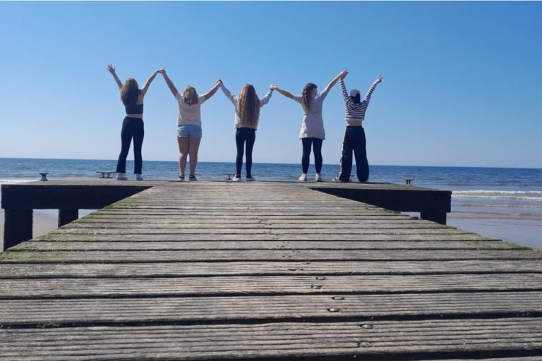 Five young people holding raised hands, looking out over the sea.