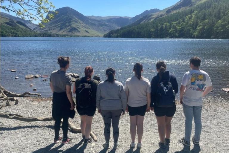 Six young people standing together looking over a lake