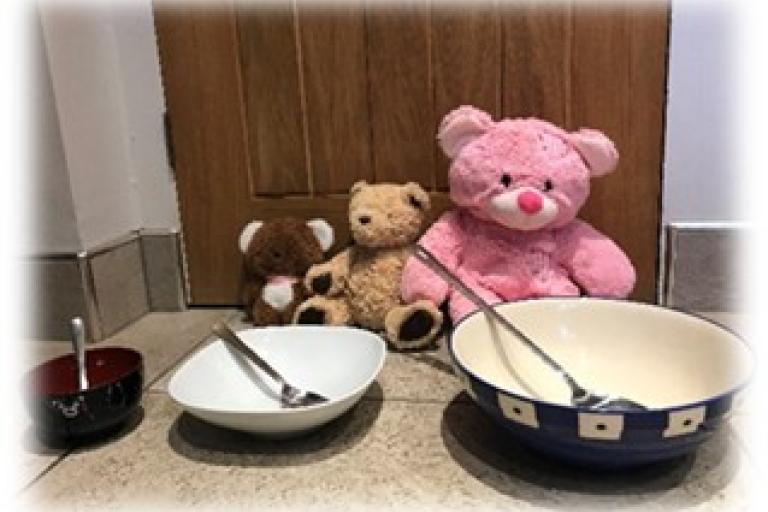Three different sized bears sat at the table with different sized plates and spoons