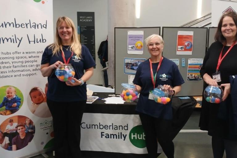 Three adults from the Hub2U team, stood in front of a stand
