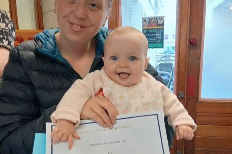 Mother holding her baby and World Breastfeeding Week certificate