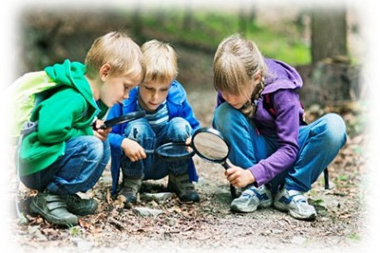 Three children crouching on the ground, using magnifying glasses to look at objects