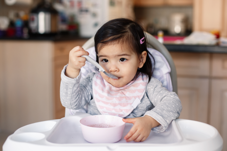 Child sat in a high chair using a spoon to feed themselves