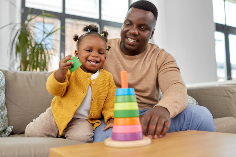 Adult and child sat on a sofa whilst child is playing with a toy