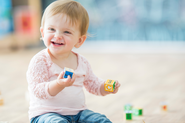 Baby sat on the floor playing with wooden bricks