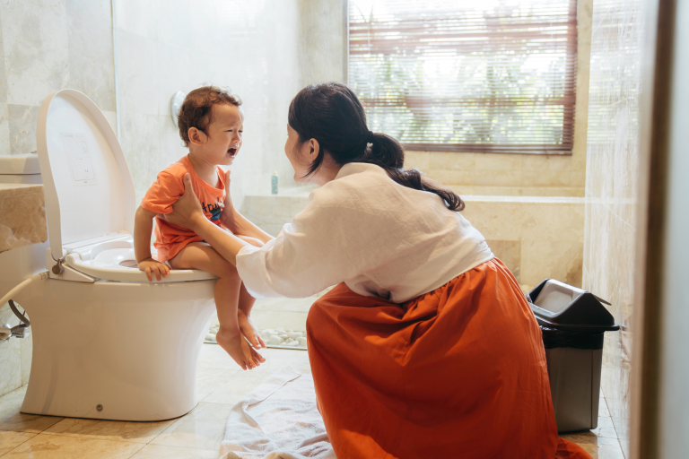 Child sat on the toilet with an adult holding them up