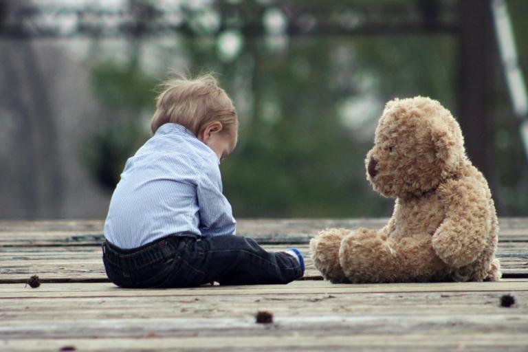 Child sat on the floor outside with their teddy