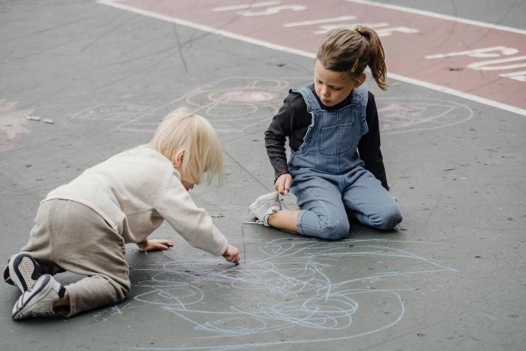 Two children drawing on the ground with chalk