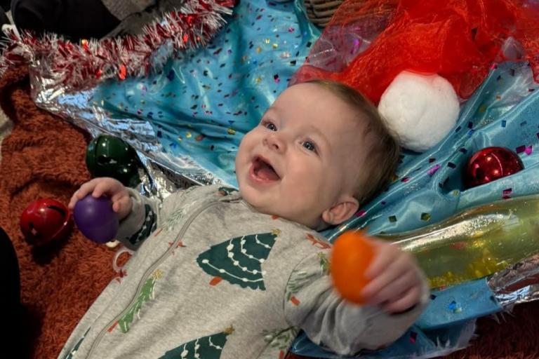 Baby in Christmas tree onesie looking excited