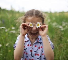Child using daisies as eyes, playing in a field