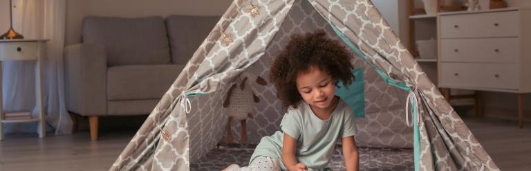 Child sat inside a homemade indoor den, reading a book