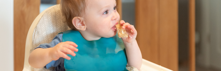 Child sat in high chair eating finger foods