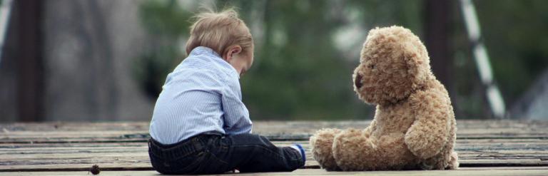 Child sat on the floor outside with their teddy