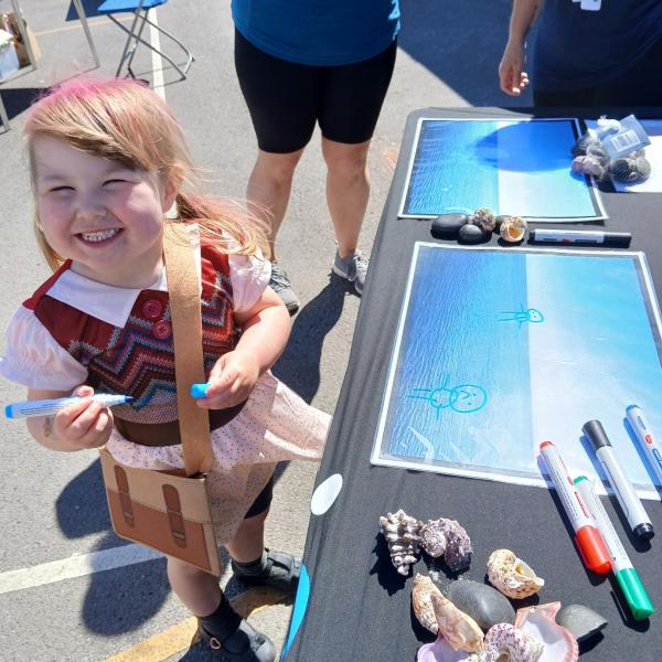 Child smiling at the camera whilst drawing a picture